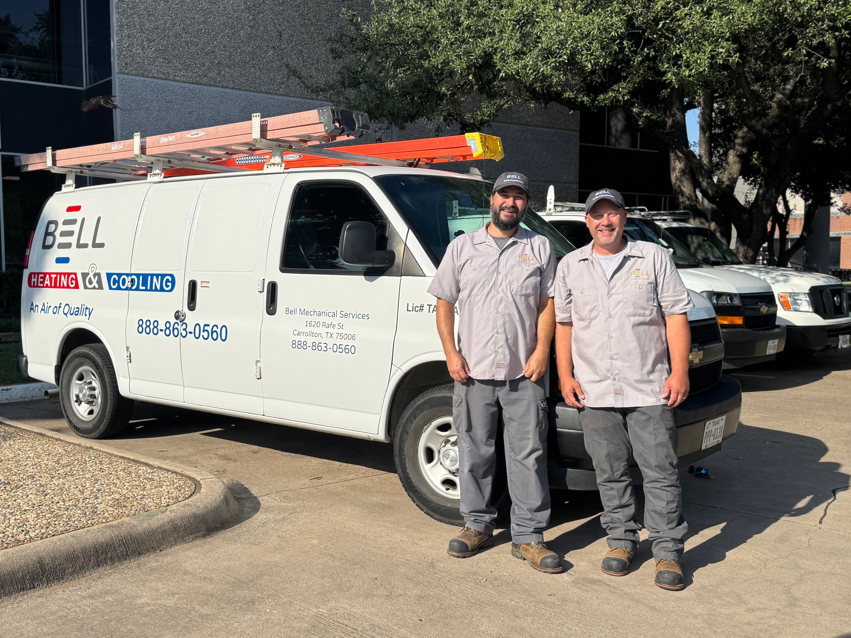 Two Bell Mechanical technicians standing beside a company service van